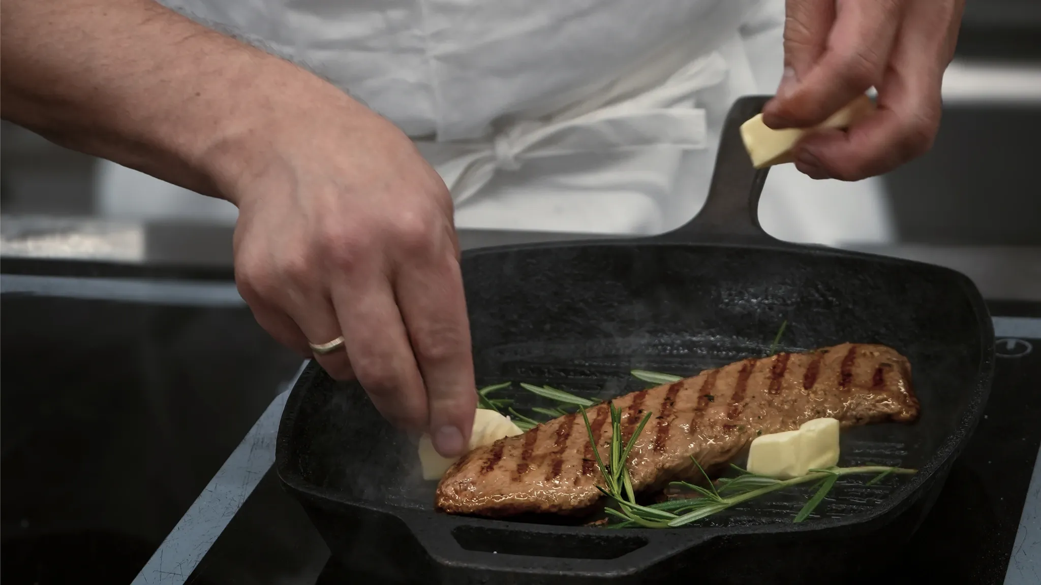 Koch legt ein Stück Butter auf ein gebratenes Fischfilet in der Pfanne.