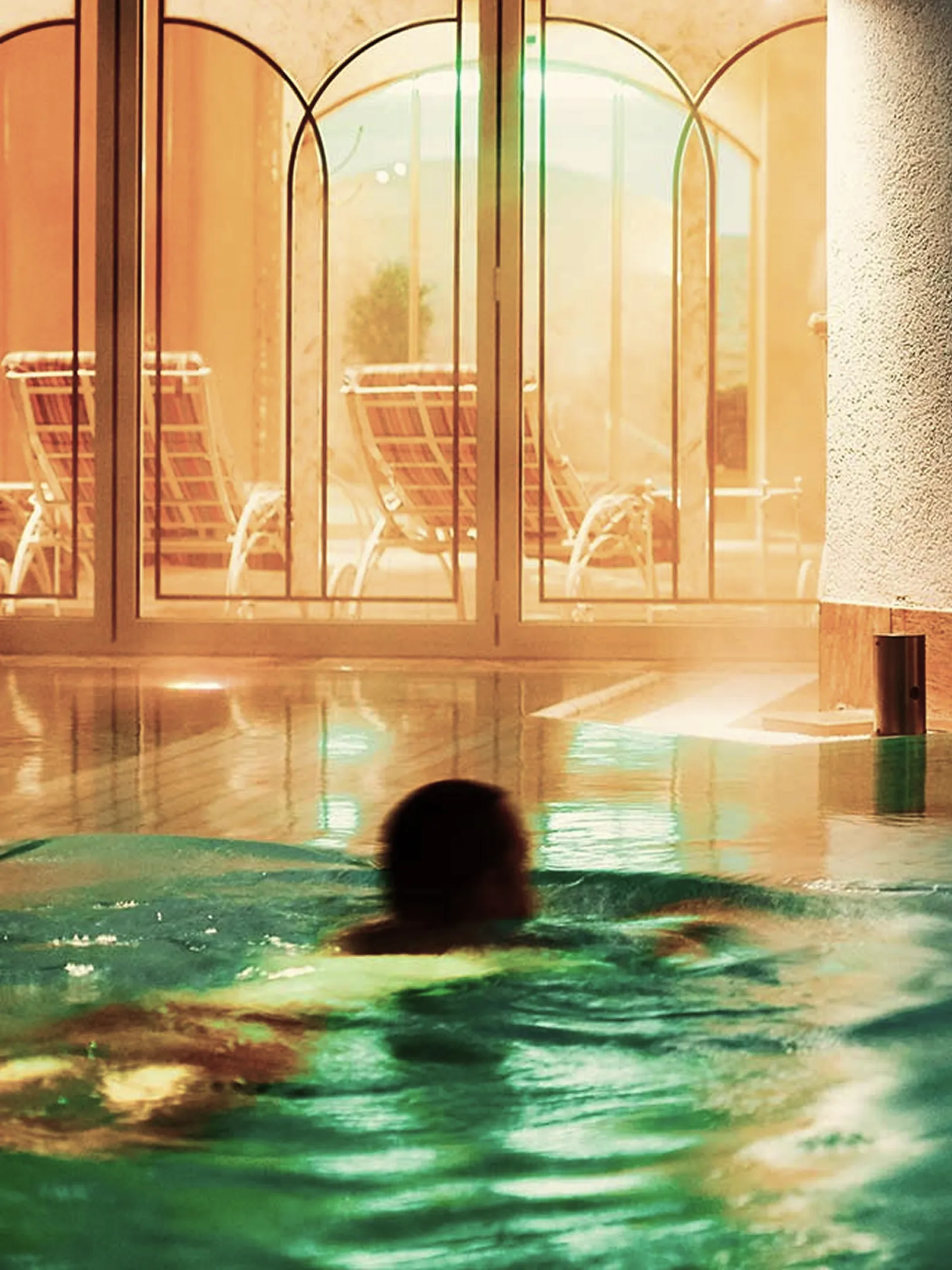 Innenpool mit türkisfarbenem Wasser und Fensterfront im warmen Abendlicht