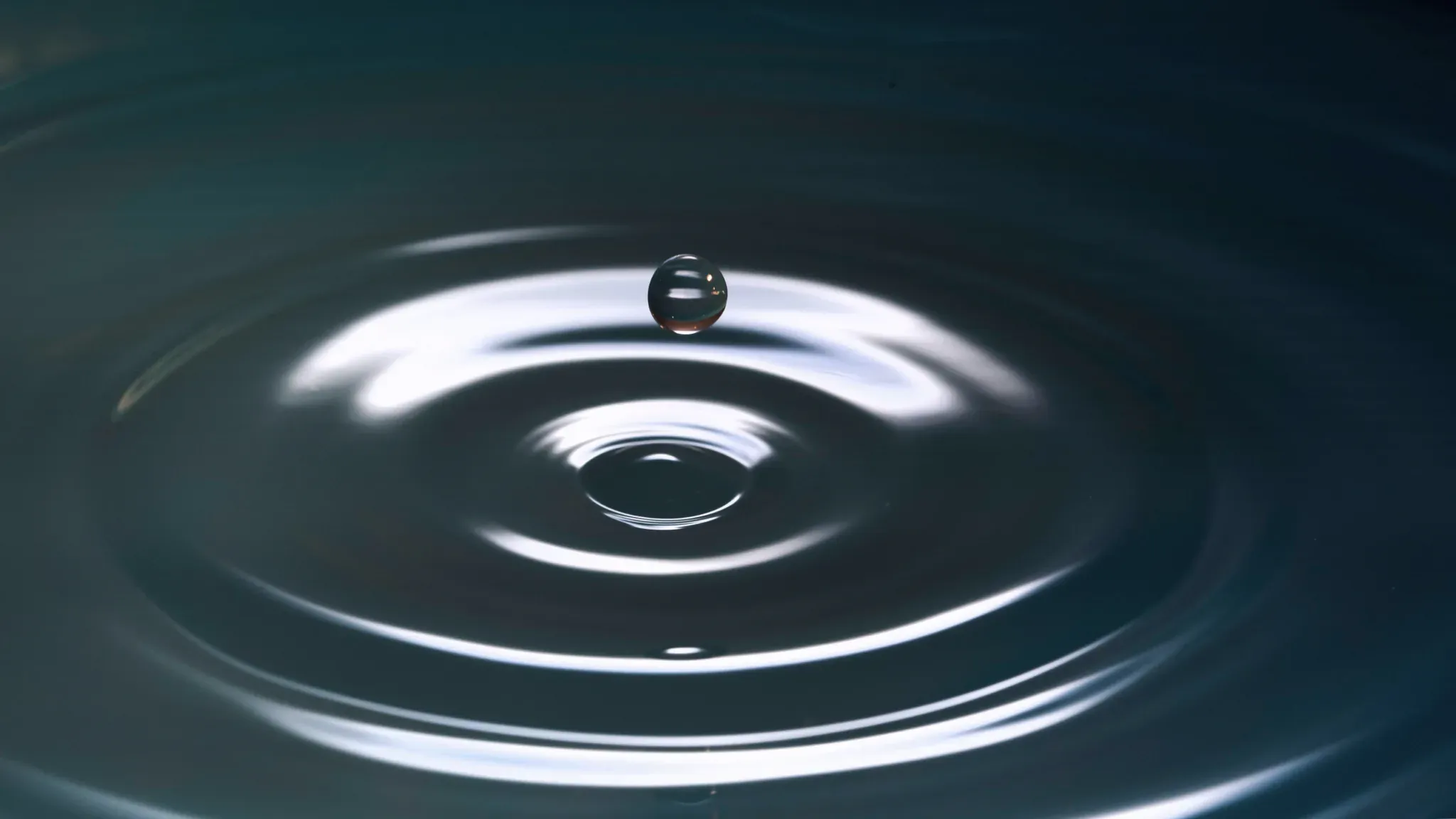 Ein Wassertropfen trifft auf eine Wasseroberfläche und bildet konzentrische Ringe.