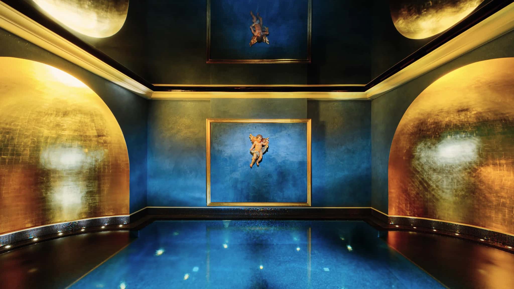 Innenpool des Engel Obertal mit blau-goldener Wandgestaltung und vergoldeter Engelsfigur, das Wasser spiegelt das Licht