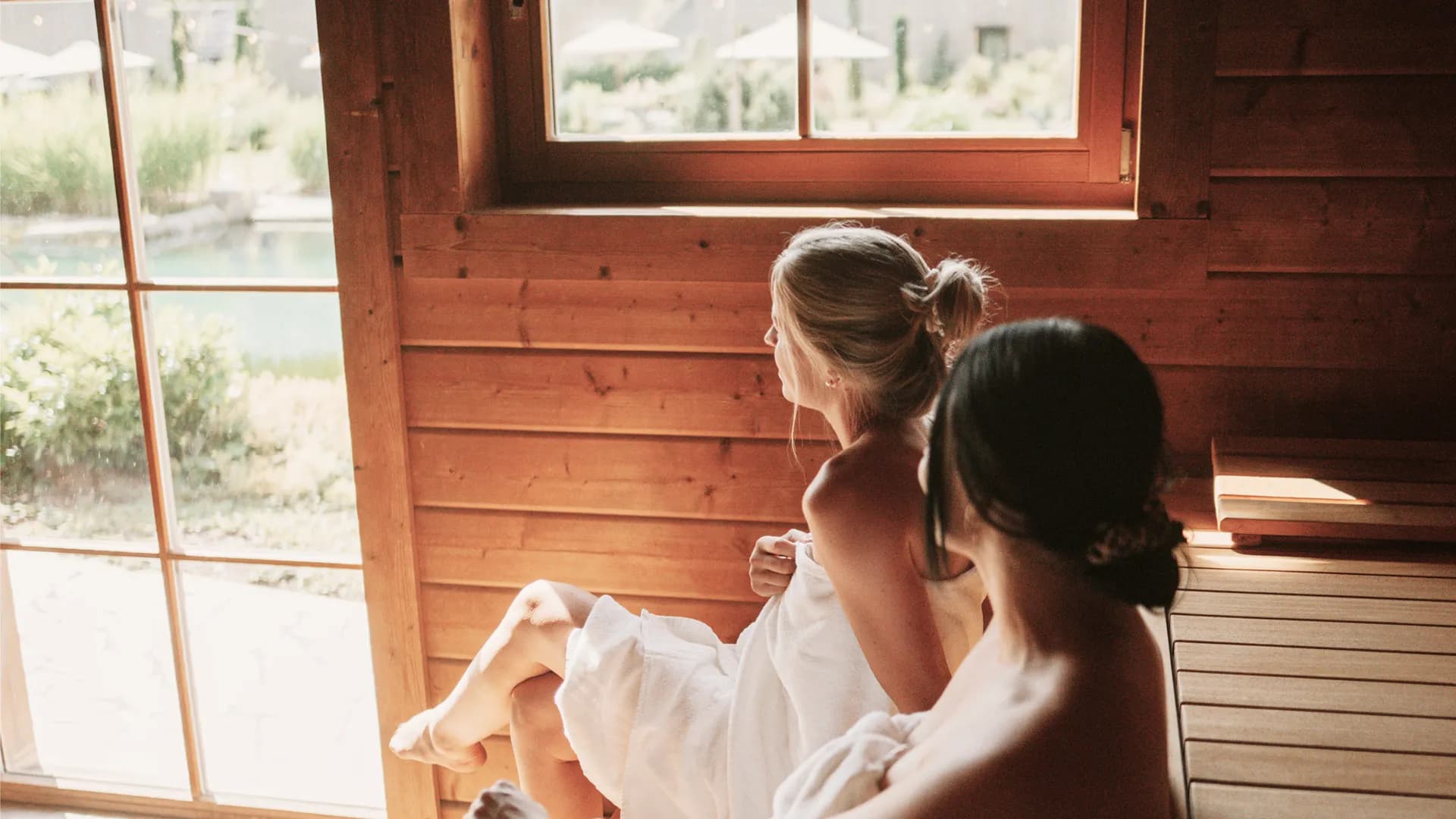 Zwei Frauen in Handtücher gehüllt sitzen in der Sauna am Panoramafenster