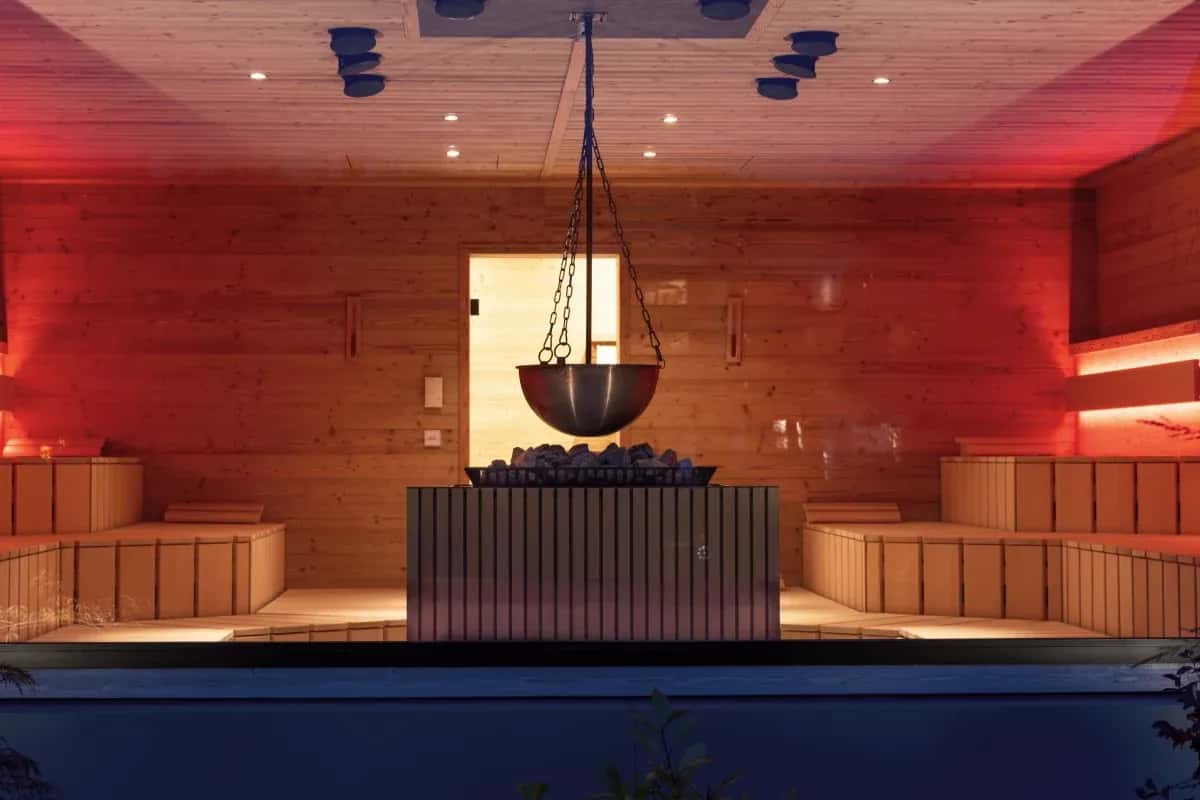 Rot beleuchtete Sauna mit hängendem Aufgusskessel und Holzbänken