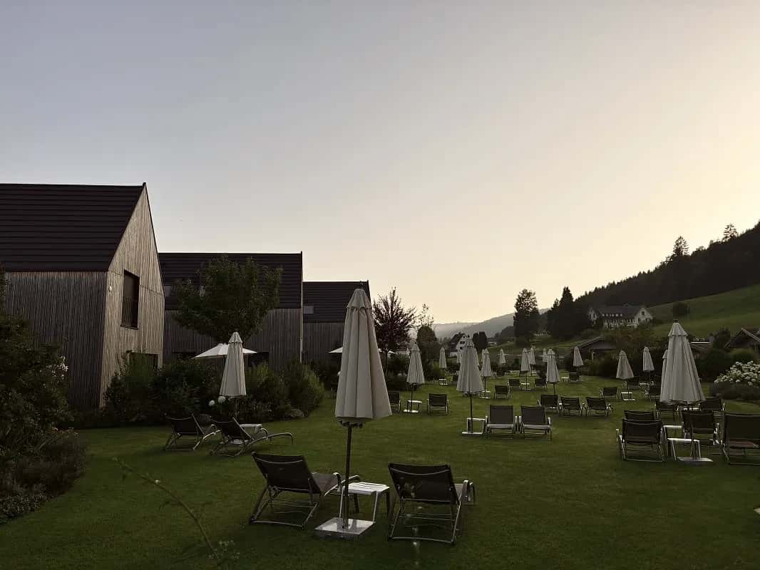 Liegewiese mit Sonnenschirmen und Liegestühlen vor Chalets in der Abenddämmerung