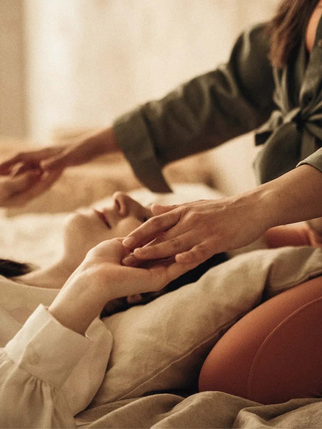 Kosmetische Behandlung: Hände einer Therapeutin an Kopf und Hand einer entspannt liegenden Person