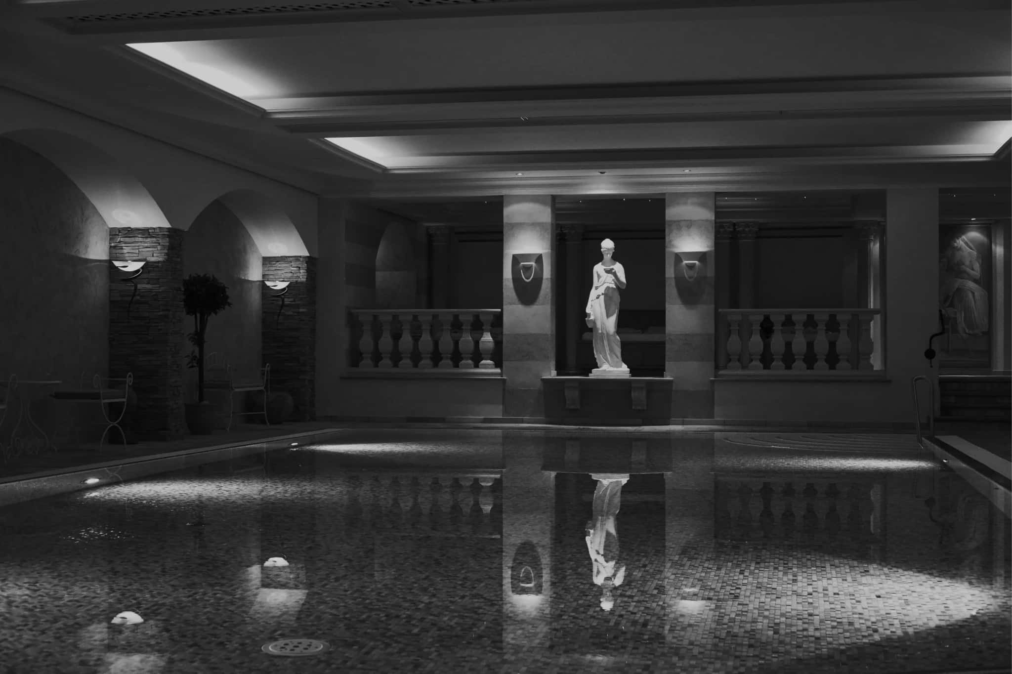 Hallenbad mit Säulen, Statue und spiegelglatter Wasserfläche, Schwarz-Weiß-Aufnahme