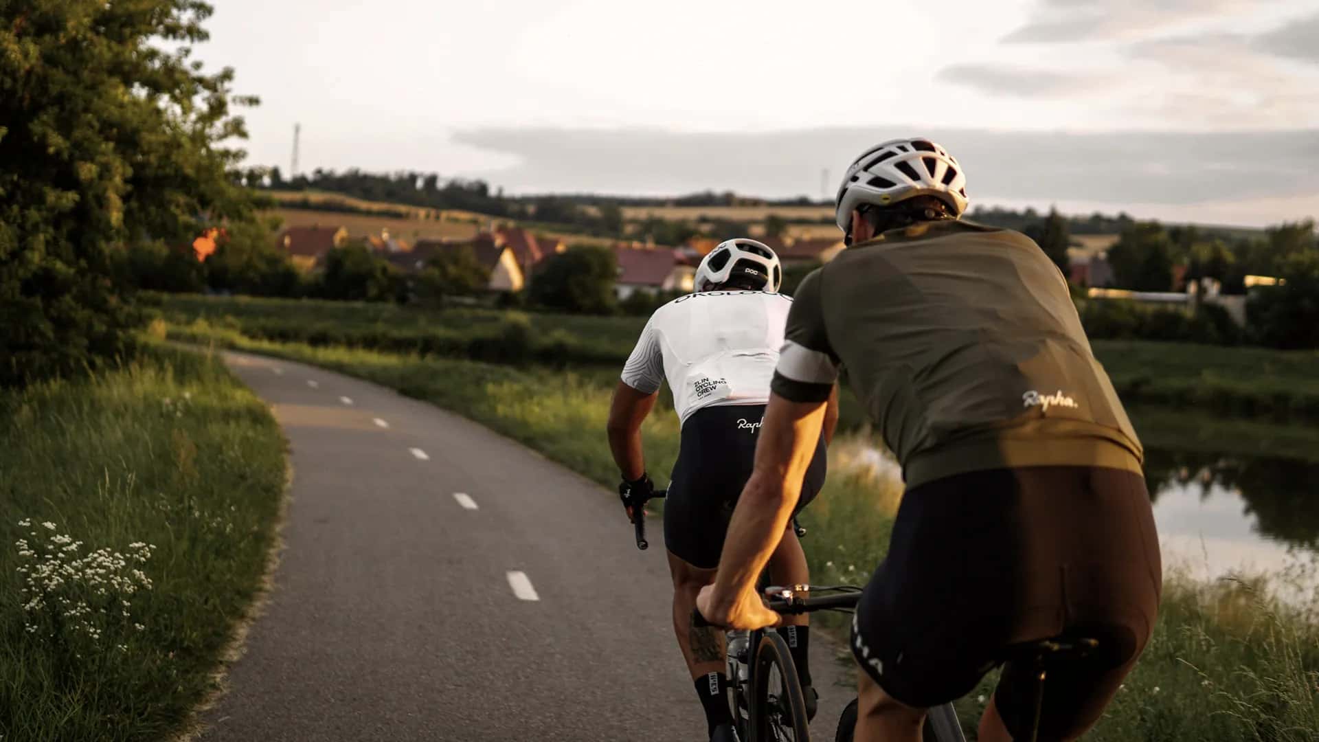 Zwei Rennradfahrer fahren nebeneinander auf einer Landstraße durch hügelige Wiesenlandschaft.
